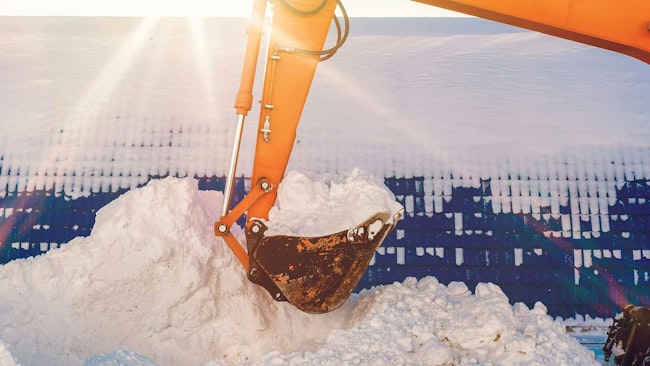 An excavator arm with hydraulic lines working in the snow