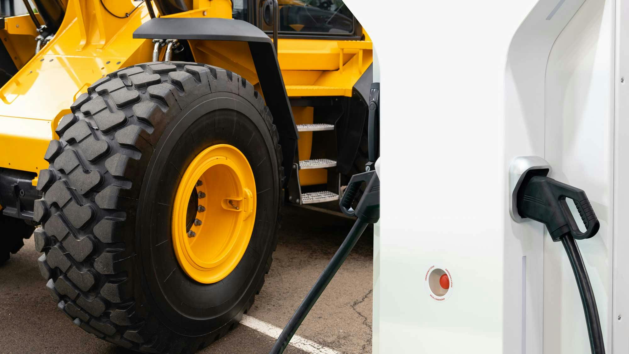 A close up on the wheels of a construction machine and an electric vehicle charger next to it