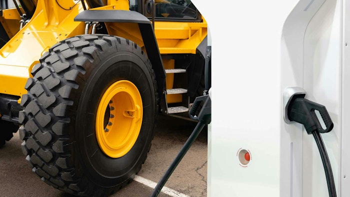 A close up on the wheels of a construction machine and an electric vehicle charger next to it