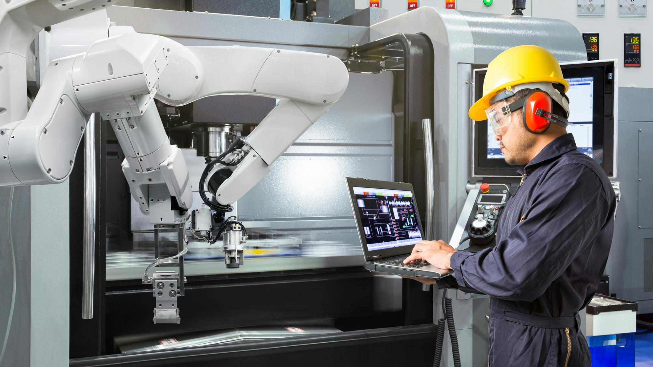A maintenance worker analyzing data on a laptop in front of an industrial robot