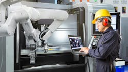 A maintenance worker analyzing data on a laptop in front of an industrial robot A maintenance worker analyzing data on a laptop in front of an industrial robot