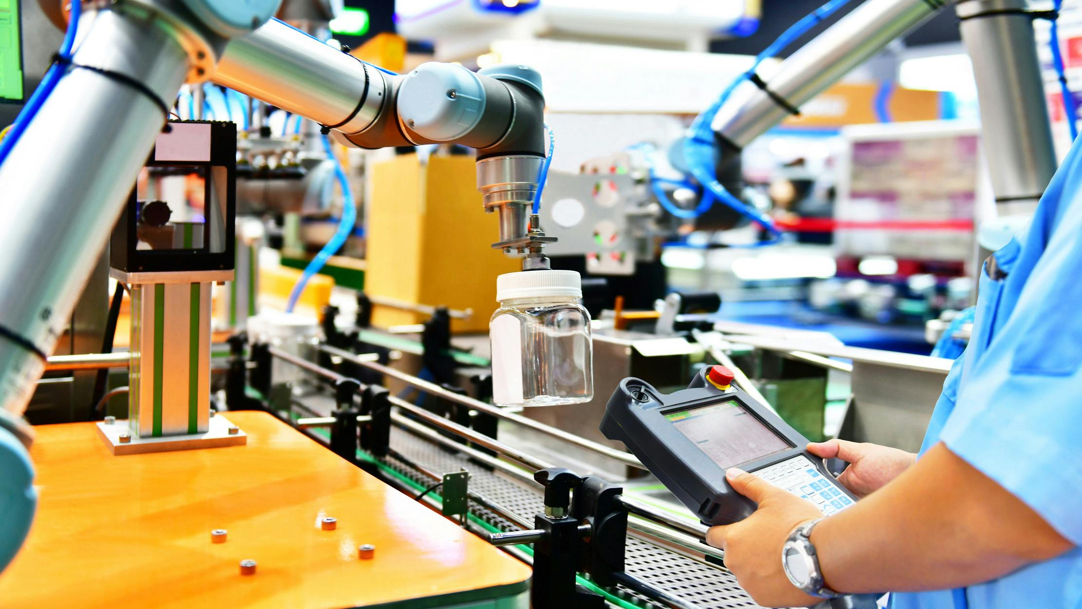 A cobot picking up a glass bottle with a human worker observing
