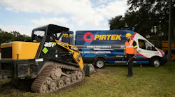 A PIRTEK technician holding a hydraulic hose walking toward a compact track loader
