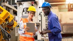 Female and male worker standing in front of industrial machinery discussing work while looking at a tablet Female and male worker standing in front of industrial machinery discussing work while looking at a tablet