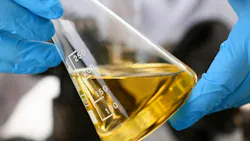 Gloved hands holding test beaker filled with oil Gloved hands holding test beaker filled with oil