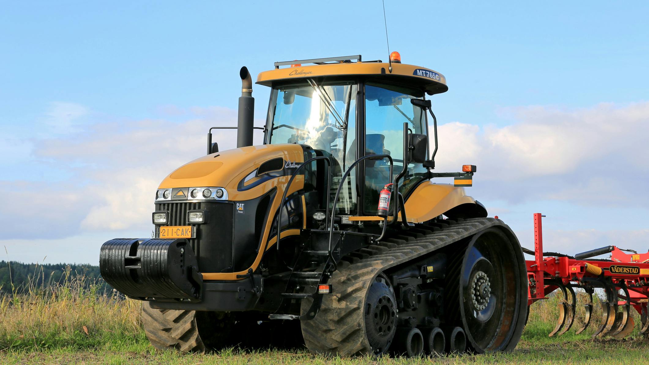 Yellow tractor pulling a red implement in a farm field