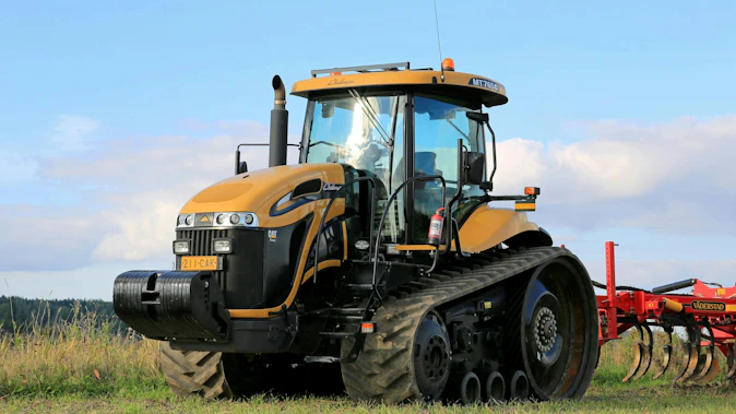 Yellow tractor pulling a red implement in a farm field