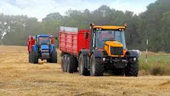 A blue and an orange tractor pulling trailers through a farm field