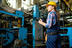 Female worker holding clipboard while looking at manufacturing machinery